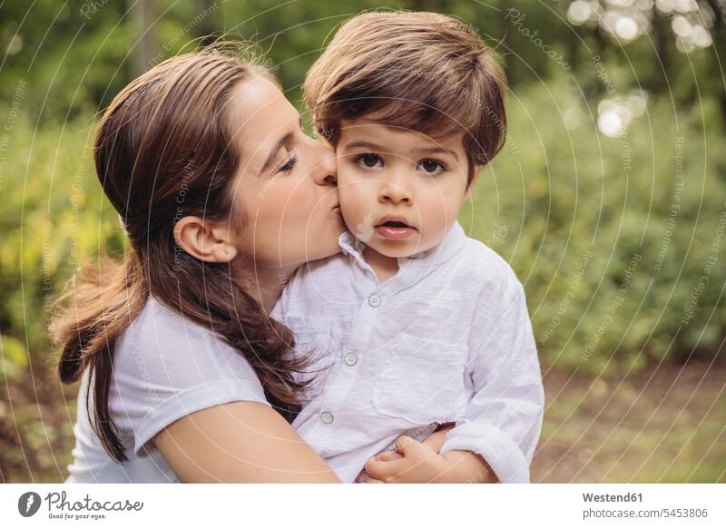 Mother kissing toddler on cheek in park portrait portraits mother mommy mothers ma mummy mama boy boys males parents family families people persons human being