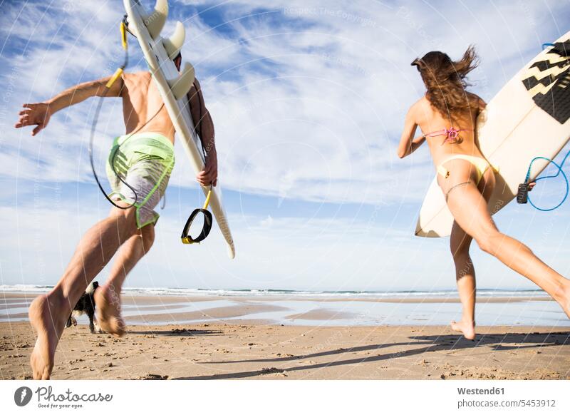 Couple carrying surfboards running on the beach surfer surfers couple twosomes partnership couples beaches surfing surf ride surf riding Surfboarding