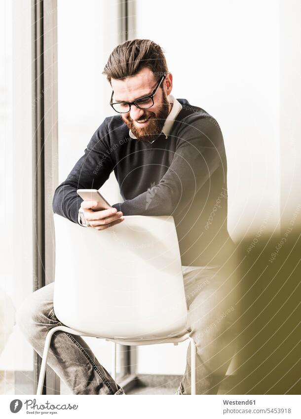 Young businessman sitting on chair using smart phone Smartphone iPhone Smartphones Businessman Business man Businessmen Business men working At Work Seated