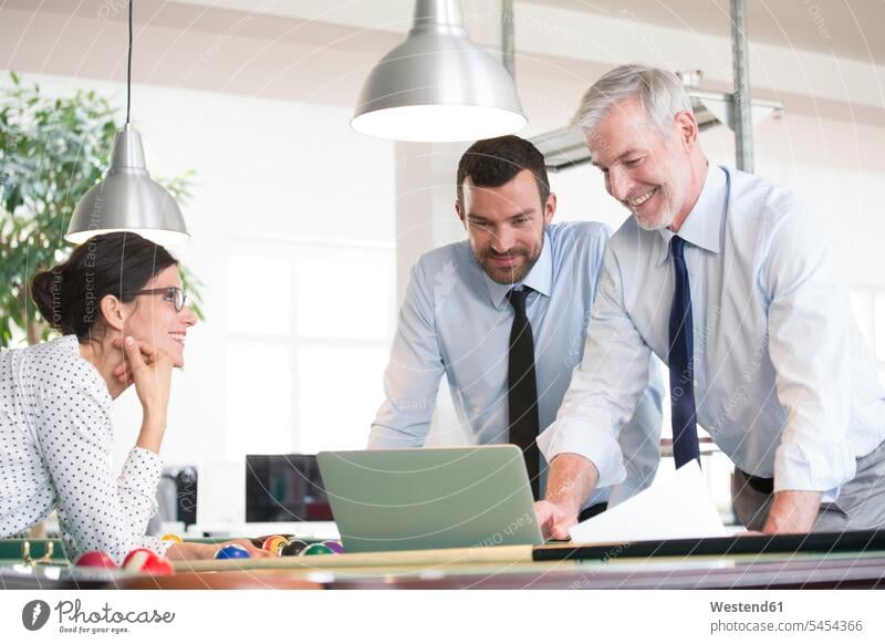 Business people standing at pool table with laptop, discussing investment strategy Laptop Computers laptops notebook business people businesspeople office