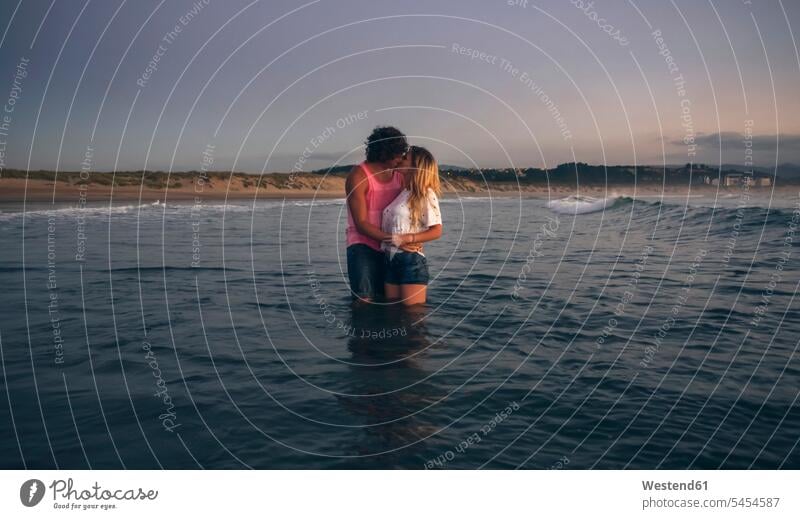 Young couple kissing in the sea at dusk kisses ocean twosomes partnership couples water waters body of water people persons human being humans human beings