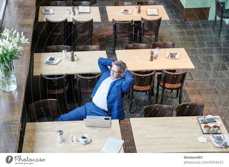 Mature businessman in cafe with laptop, cell phone and earbuds Laptop Computers laptops notebook Businessman Business man Businessmen Business men hearing