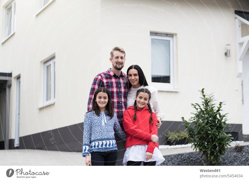 Portrait of parents and twin daughters in front of their family home home ownership private owned home families portrait portraits smiling smile