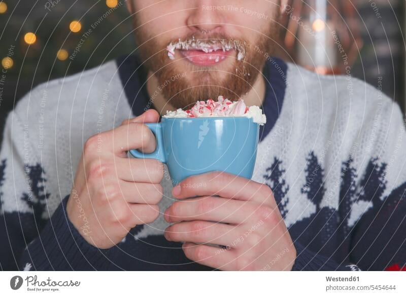 Man drinking hot chocolate with whipped cream and chopped candy canes at Christmas time smeared smudged Cream holding hand human hand hands human hands Cocoa
