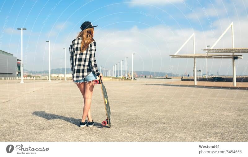 Back view of young woman with longboard standing in front of beach promenade, partial view females women Adults grown-ups grownups adult people persons