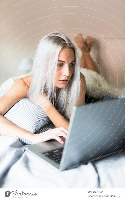 Young woman lying in bed using laptop laying down lie lying down beds Laptop Computers laptops notebook females women computer computers Adults grown-ups