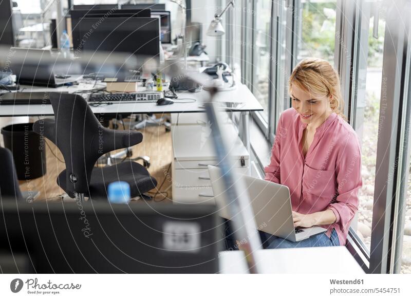 Smiling woman using laptop in office Laptop Computers laptops notebook smiling smile offices office room office rooms females women computer computers workplace