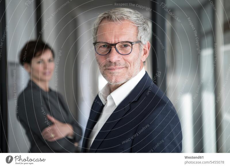 Portrait of confident businessman with businesswoman in background Businessman Business man Businessmen Business men portrait portraits business people