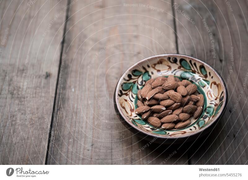 Almonds in hand-painted bowl on wood Nut Nuts close-up close up closeups close ups close-ups large group of objects many objects wooden healthy eating nutrition