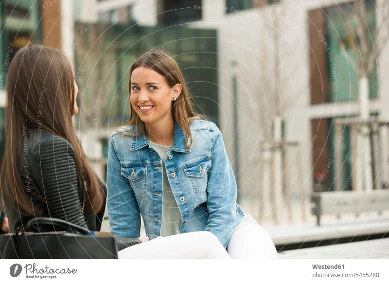 Girlfriends sitting on a bench, chatting meeting encounter gathering Gossip gossiping Chitchat Buzz Seated talking speaking laughing Laughter happiness happy