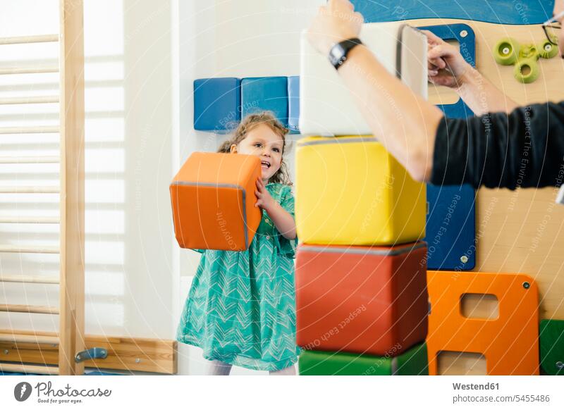 Happy little girl lifting up a soft building block in gym room of a kindergarten child children kid kids playing females girls nursery school people persons
