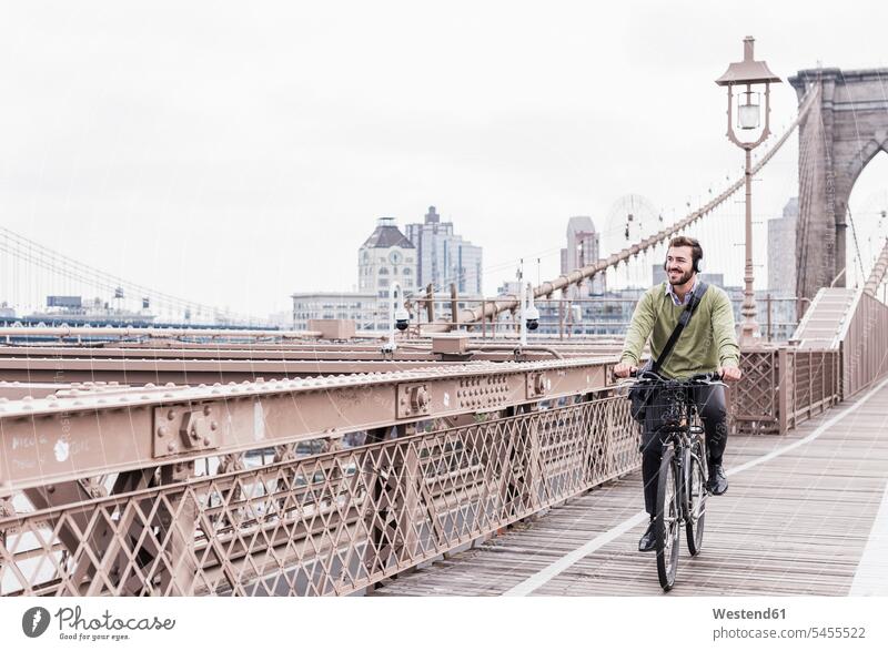 USA, New York City, man on bicycle on Brooklyn Bridge New York State headphones headset smiling smile bridge bridges bikes bicycles men males United States