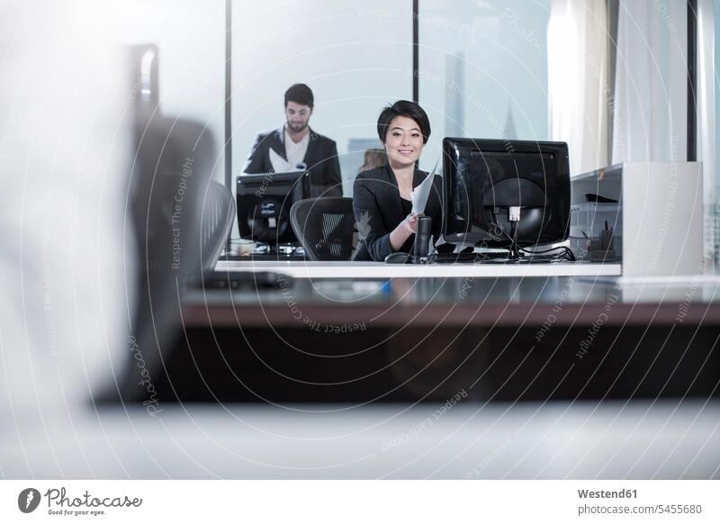 Smiling woman sitting at desk in city office offices office room office rooms females women smiling smile working At Work businesswoman businesswomen