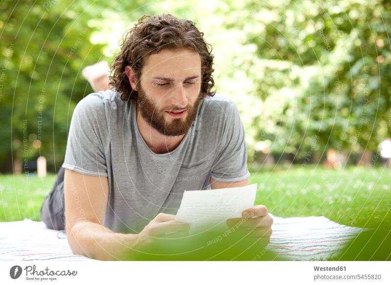 Man lying on blanket in a park reading a letter man men males letter document letters Adults grown-ups grownups adult people persons human being humans