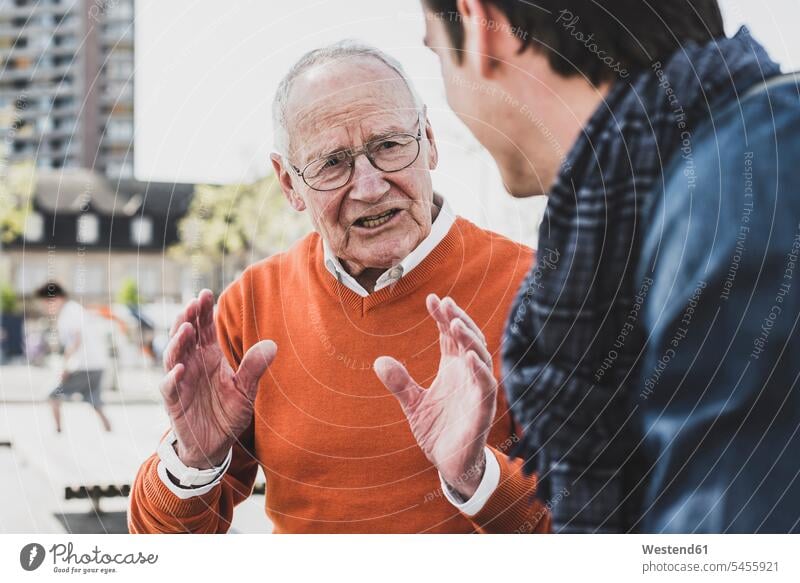 Senior man talking to adult grandson outdoors grandsons speaking grandfather grandpas granddads grandfathers grandchild grandchildren family families people