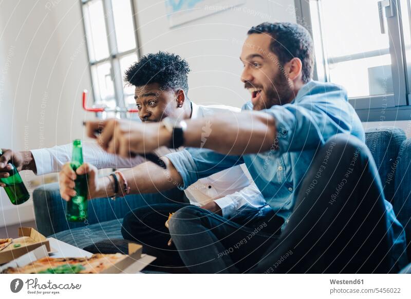 Excited friends with beer bottles sitting on the sofa cheering Beer Beers Ale fan admirer fans happiness happy couch settee sofas couches settees Seated