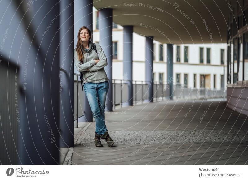 Smiling young woman leaning against column looking at distance females women Adults grown-ups grownups adult people persons human being humans human beings