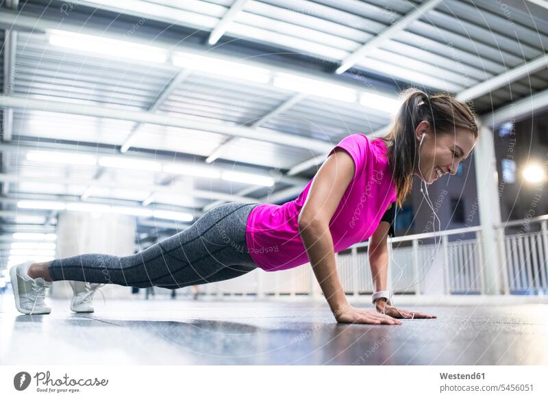 Smiling young woman in pink sportshirt stretching in modern metro station at night exercising exercise training practising jogger joggers female jogger