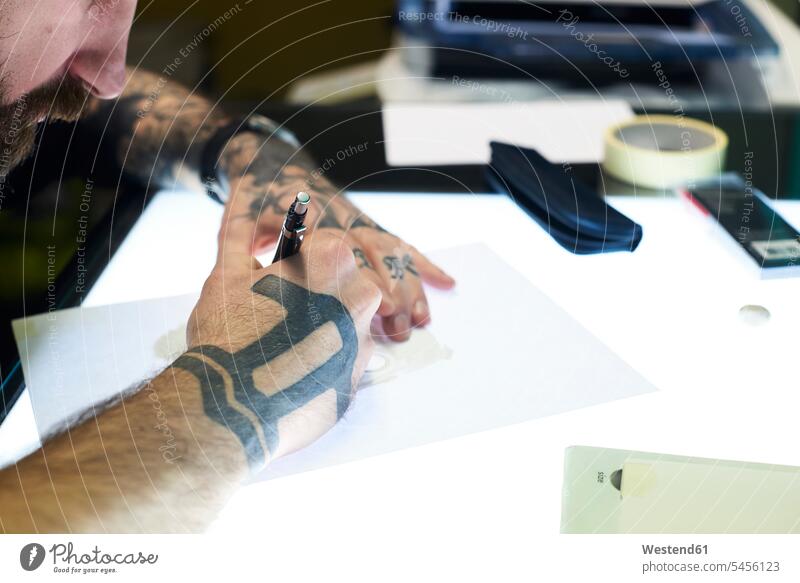 Tattoo artist designing motif on light table in studio sketch tattoo tattoos man men males drawing sketching tattooist tattooer tattooed body art Body Adornment