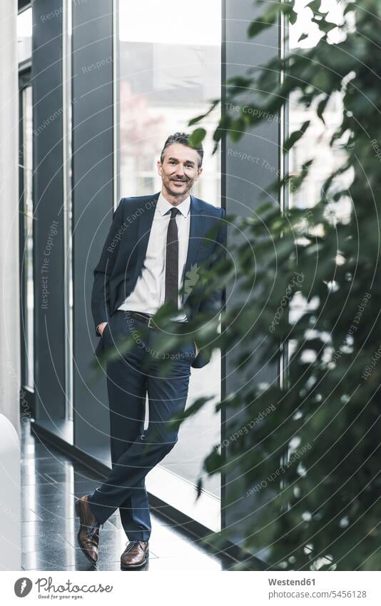 Portrait of smiling businessman standing in office lobby lobbies portrait portraits offices office room office rooms smile Businessman Business man Businessmen