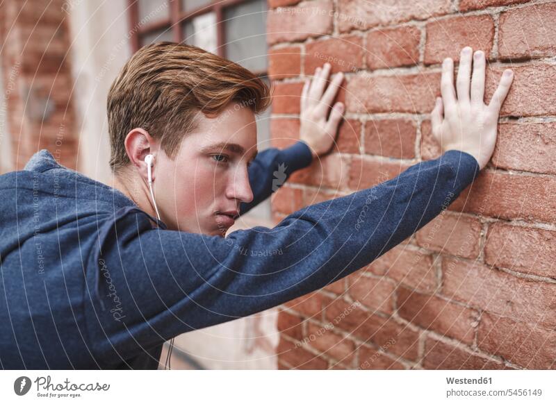 Young man with earphones leaning against brick building men males ear phone ear phones serious earnest Seriousness austere hearing Adults grown-ups grownups