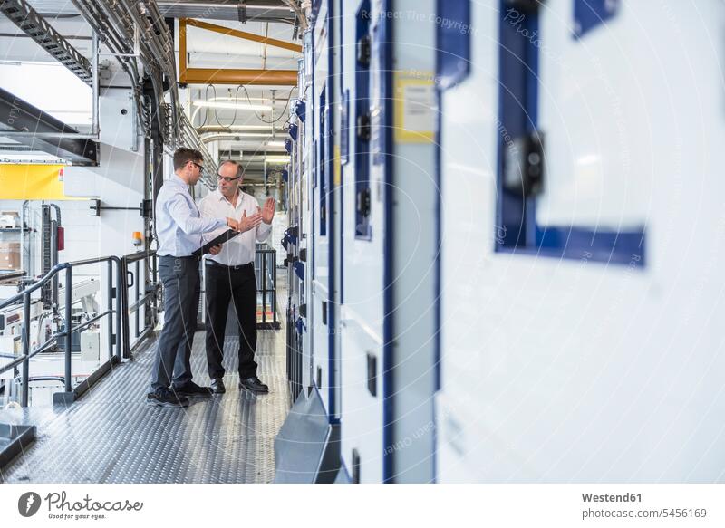 Two men talking in factory shop floor speaking man males colleagues factories Adults grown-ups grownups adult people persons human being humans human beings