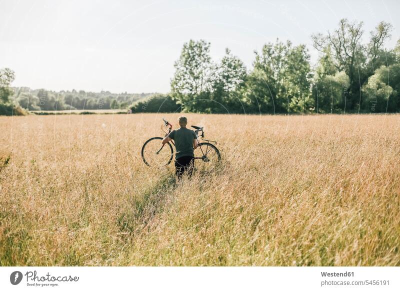 Young man carrying his bike, field men males cyclist leisure free time leisure time Field Fields farmland bicycle bikes bicycles Adults grown-ups grownups adult