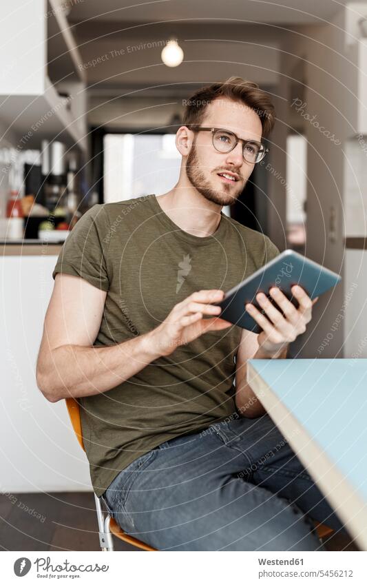 Young man with tablet sitting in kitchen at home digitizer Tablet Computer Tablet PC Tablet Computers iPad Digital Tablet digital tablets portrait portraits