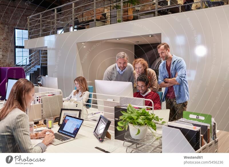 Colleagues looking over shoulder of young man working in modern office offices office room office rooms PC desktop PC personal computers desktop computer