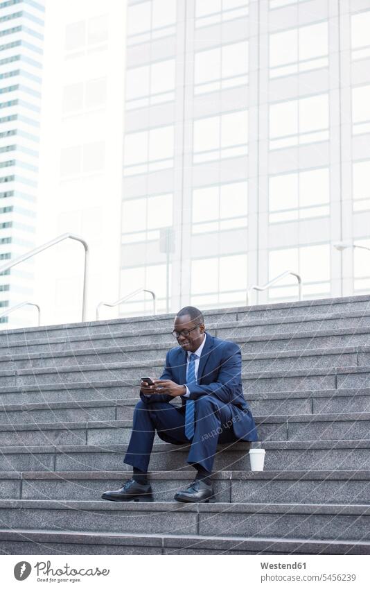 Businessman sitting on stairs with cell phone and takeaway coffee mobile phone mobiles mobile phones Cellphone cell phones stairway Business man Businessmen