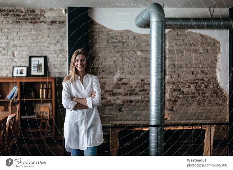 Young woman standing in coffee shop with arms crossed owner owners cafe young females women startup young business start up startup company startups