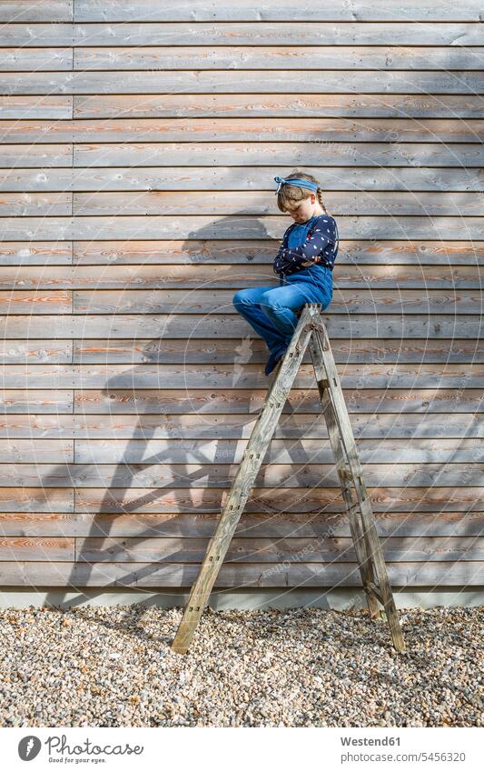Girl sitting on ladder in front of a wooden facade pouting mouth ladders Seated girl females girls child children kid kids people persons human being humans