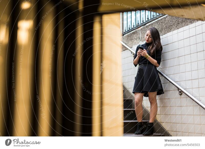 USA, New York City, Manhattan, young woman standing on stairs looking at smartphone Smartphone iPhone Smartphones females women mobile phone mobiles