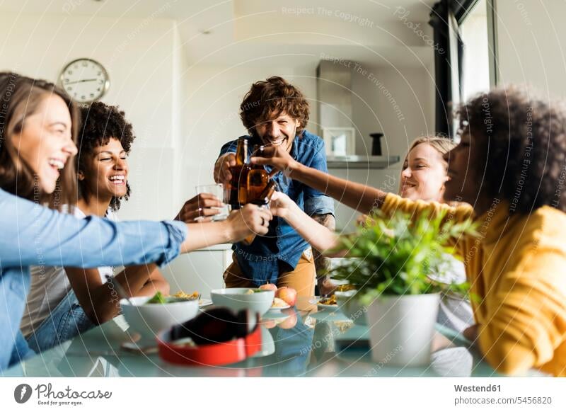 Cheerful friends clinking beer bottles at dining table Beer Beers Ale toasting cheers cheerful gaiety Joyous glad Cheerfulness exhilaration merry gay