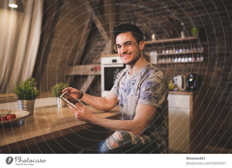 Portrait of smiling young man using tablet in kitchen at home portrait portraits domestic kitchen kitchens digitizer Tablet Computer Tablet PC Tablet Computers