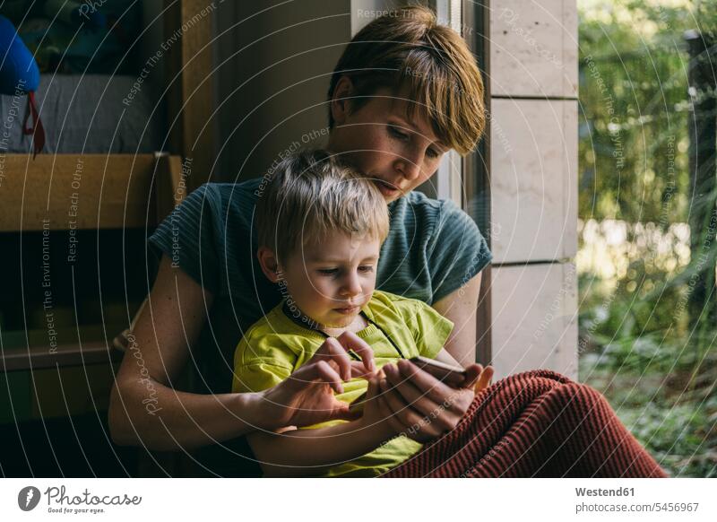 Mother and little son cuddling at home looking at smartphone human human being human beings humans person persons families mama mom mommy mothers mummy Blankets