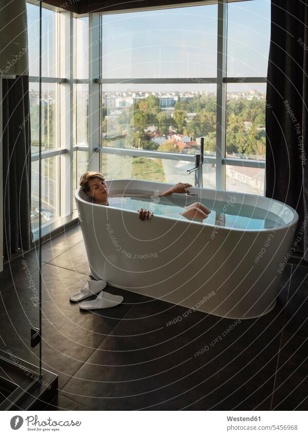 Woman taking bath in bathtub against window at luxury hotel room color image colour image indoors indoor shot indoor shots interior interior view Interiors day
