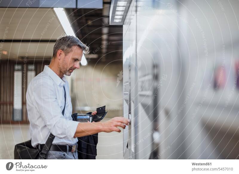 Businessman withdrawing money through ATM machine at station color image colour image Germany Businessmen Business man Business men businesswear business attire