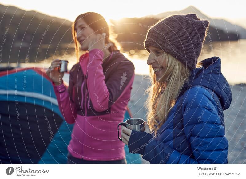 Two female friends at tent holding mugs tents cup mate friendship leisure free time leisure time Quality Time evening in the evening focus on foreground