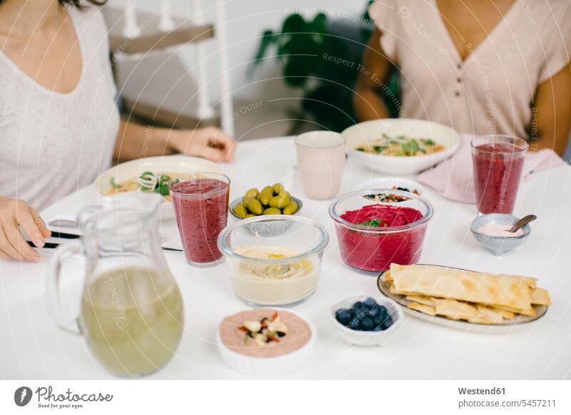 Two women sitting at table having a healthy meal friends mate female friend Drinking Glass Drinking Glasses Bowls dish dishes Plates Tables Dining Tables