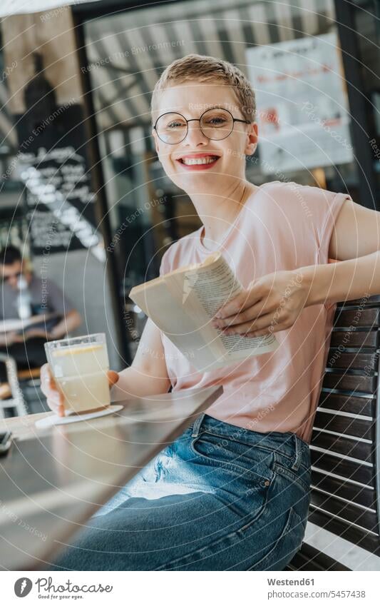 Smiling mid adult woman reading book while sitting in sidewalk with coffee drink on sunny day color image colour image outdoors location shots outdoor shot