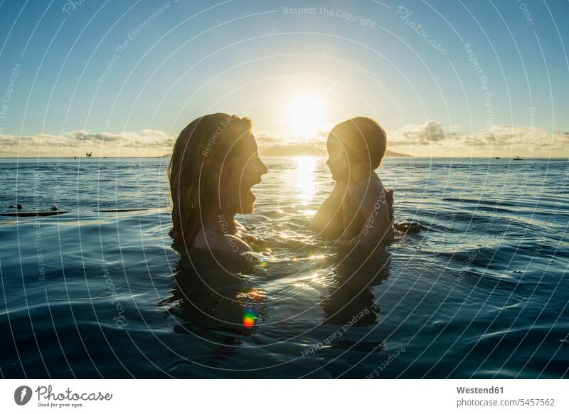 French Polynesia, Tahiti, Papeete, woman playing with her little baby in an infinity pool at sunset Infinity Pool Moody Sky Lens Flare Lens Flares Lensflare