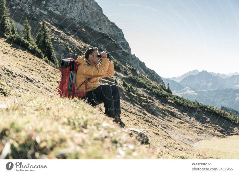 Austria, Tyrol, man having a break during a hiking trip in the mountains looking through binoculars hiking tour walking tour mountain range mountain ranges men