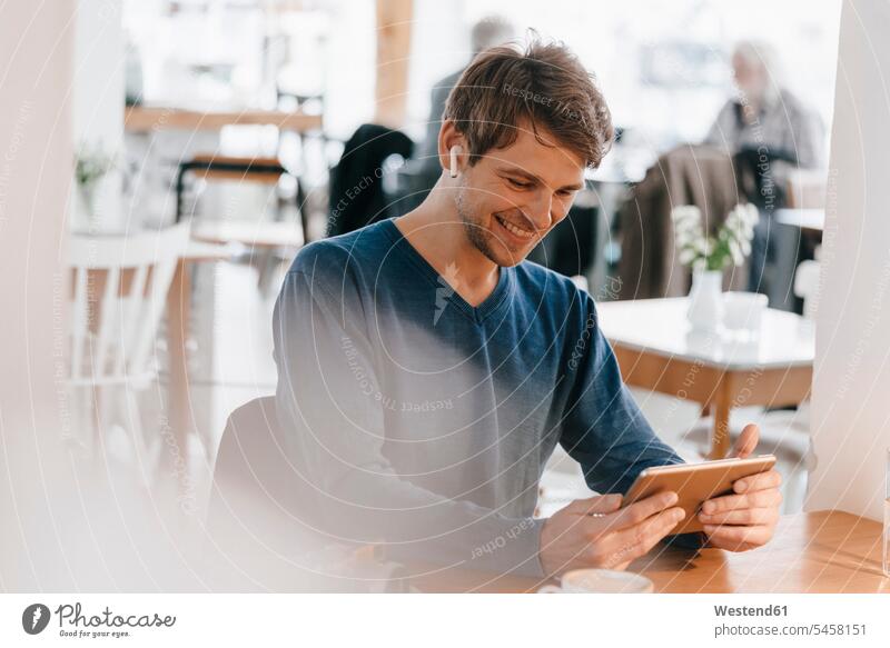 Smiling man in a cafe with earphone using tablet earphones ear phone ear phones smiling smile digitizer Tablet Computer Tablet PC Tablet Computers iPad