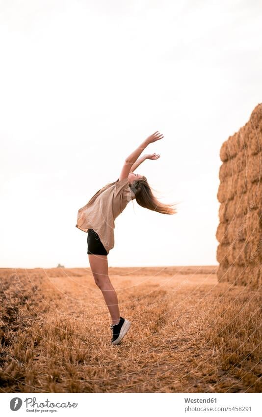 Happy young woman jumping in field females women cheering jubilate rejoicing rejoice exultation jubilating beautiful Field Fields farmland Hay hay bale