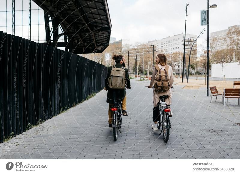 Rear view of couple riding e-bikes in the city talking to each other riding bicycle riding bike bike riding cycling bicycling pedaling bicycles speaking