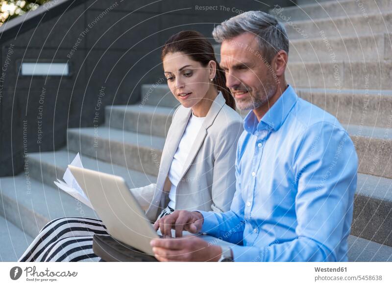 Two business people sitting side by side on stairs working together paralell Juxtaposed in paralell At Work businesspeople Seated stairway business world