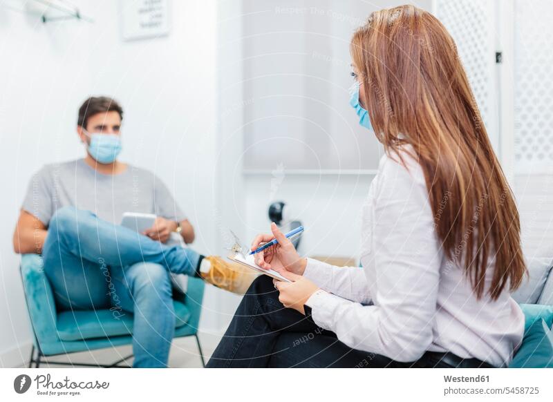 Doctor writing in notepad while listening to patient problem at office color image colour image indoors indoor shot indoor shots interior interior view