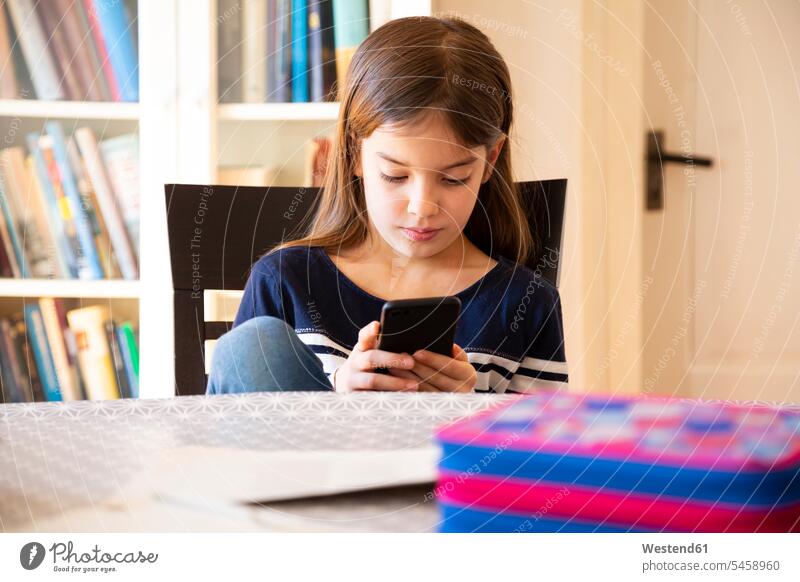 Girl doing homework with smartphone rack racks Shelve shelves book shelf Book Shelves bookshelves Tables phones telephone telephones cell phone cell phones