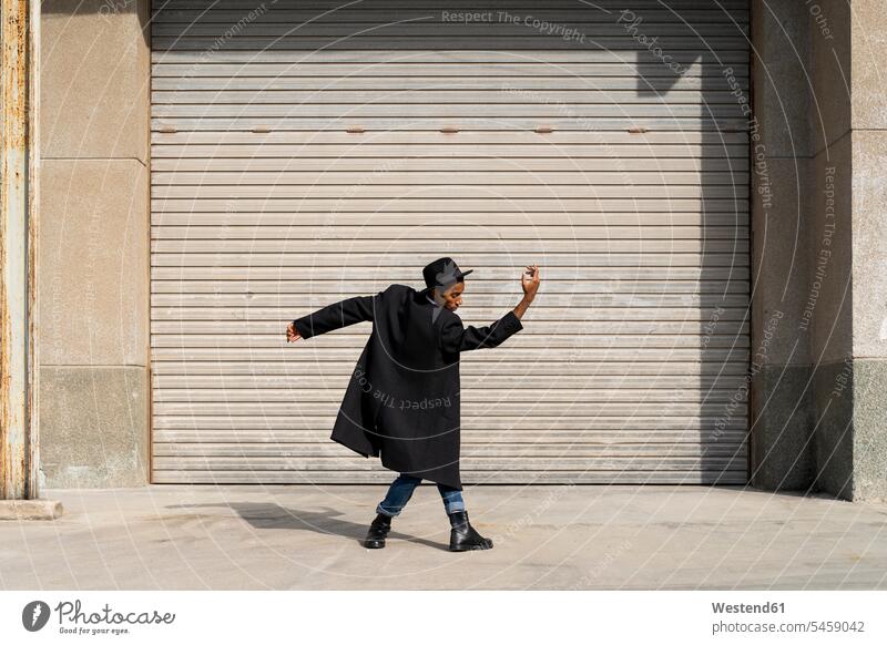 Carefree young man enjoying day by dancing against shutter on sunny day color image colour image outdoors location shots outdoor shot outdoor shots